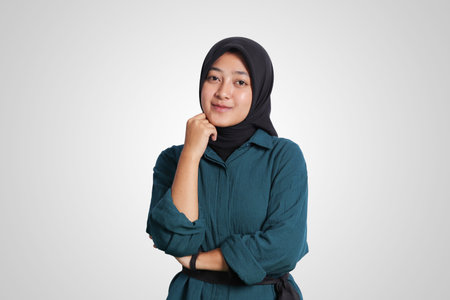 Portrait of excited Asian muslim woman with hijab holding hand near face while looking at camera, beauty pose concept. Isolated image on white backgroundの写真素材