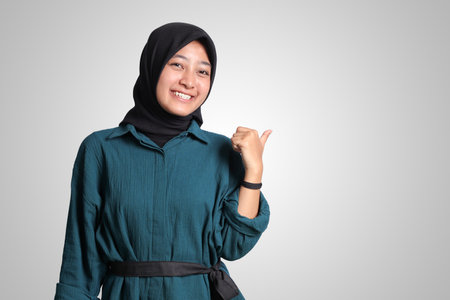 Portrait of excited Asian muslim woman with hijab showing thumb up hand gesture, saying good job. Advertising concept. Isolated image on white backgroundの写真素材