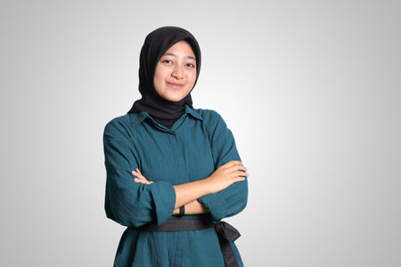 Portrait of cheerful Asian muslim woman with hijab, keeping arms crossed and smiling looking at camera. Isolated image on white backgroundの写真素材