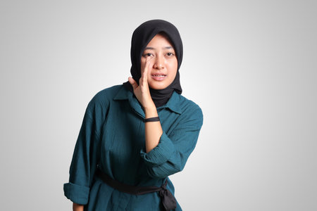 Portrait of cheerful Asian woman with hijab, trying to hear gossip or sound, holding hand near ear and listening carefully. Advertising concept. Isolated image on white backgroundの写真素材