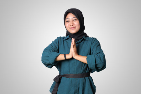 Portrait of cheerful Asian woman hijab in casual shirt, showing apologize and welcome hand gesture. Advertising concept. Isolated image on white backgroundの写真素材