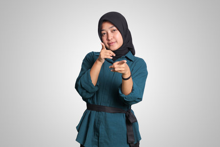 Portrait of excited Asian hijab woman in casual outfit standing against white background, showing product and pointing with hand and finger to the side. Advertising concept.の写真素材