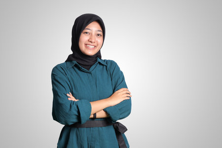 Portrait of cheerful Asian muslim woman with hijab, keeping arms crossed and smiling looking at camera. Isolated image on white backgroundの写真素材