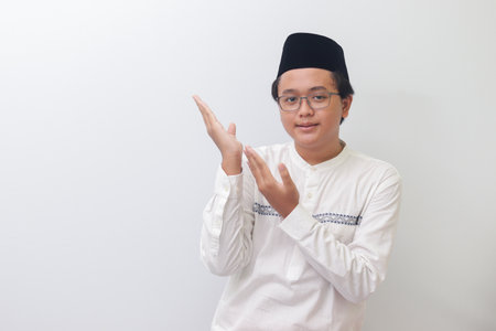 Portrait of young Asian muslim man showing product and pointing with his hand and finger. Isolated image on white backgroundの写真素材
