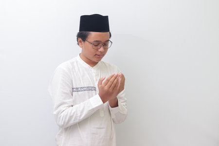 Portrait of young millennial Asian muslim man praying earnestly with his hands raised. Isolated image on white backgroundの写真素材