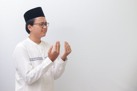 Portrait of young millennial Asian muslim man praying earnestly with his hands raised. Isolated image on white backgroundの写真素材