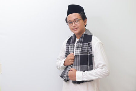 Portrait of young Asian muslim man standing with cool pose and holding his sarong. Isolated image on white backgroundの写真素材