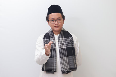 Portrait of young Asian muslim man reaching out his hand for a handshake. Isolated image on white backgroundの写真素材