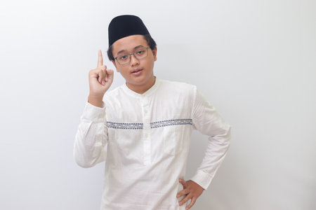 Portrait of young Asian muslim man pointing up his forefinger and reminding something to do. Advertising concept. Isolated image on white backgroundの写真素材