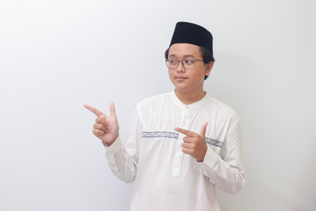 Portrait of young Asian muslim man showing product and pointing with his hand and finger. Isolated image on white backgroundの写真素材