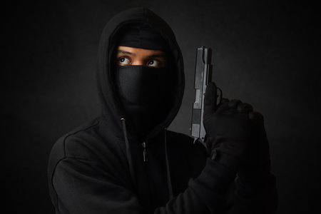 Mysterious man wearing black hoodie and mask holding a pistol