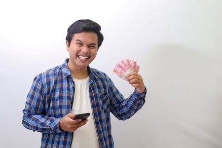 Portrait of excited Asian man in blue plaid shirt standing against white background, showing one...