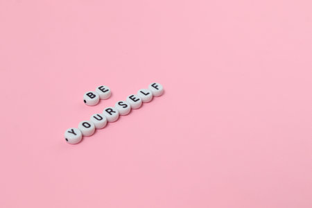 Top view of be yourself quotes made out of beads on pink background. motivation and success concept