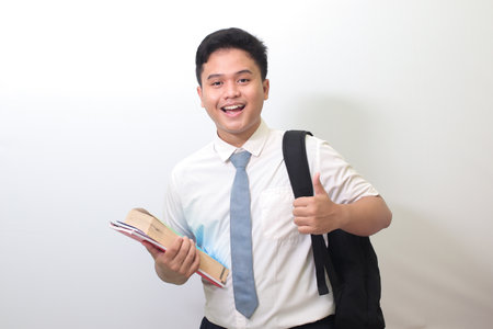 Indonesian senior high school student wearing white shirt uniform with gray tie showing good job hand gesture, thumb up finger. Isolated image on white backgroundの写真素材