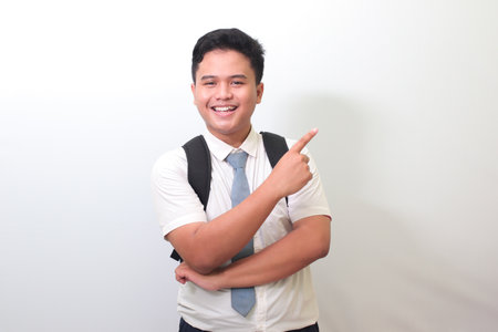 Indonesian senior high school student wearing white shirt uniform with gray tie showing product, pointing at something and smiling. Isolated image on white backgroundの写真素材