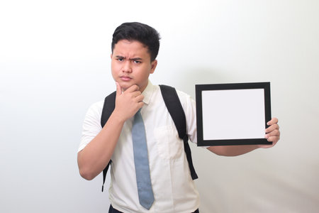 Indonesian senior high school student wearing white shirt uniform with gray tie showing empty frame with confusion expression. Blank space for typography or text to fillの写真素材
