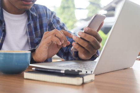 Close up of freelance male hand working on laptop while using a mobile phone. Business and mockup conceptの写真素材