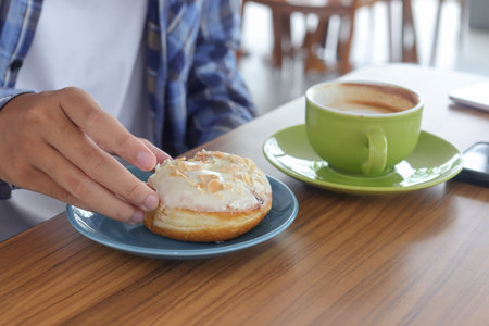 Close up of male hand eating sweet donut in cafeの写真素材