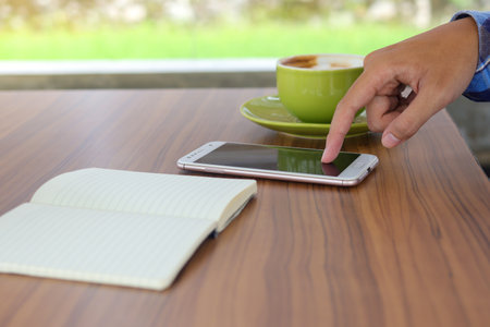 Close up of male finger touching smartphone screen in cafeの写真素材