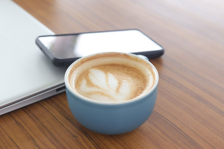 a cup of latte coffee with smartphone on back in cafeの写真素材
