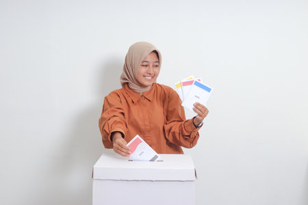 Portrait of Asian hijab woman inserting and putting the voting paper into the ballot box. General elections or Pemilu for the president and government of Indonesia. Isolated image on white backgroundの写真素材