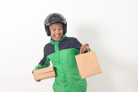 Portrait of Asian online courier driver wearing green jacket and helmet giving craft paper shopping...