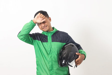Portrait of tired Asian online taxi driver wearing green jacket holding a helmet on hip and feeling exhausted. Isolated image on white backgroundの写真素材