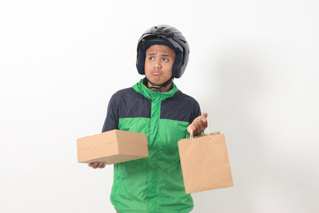 Portrait of Asian online courier driver wearing green jacket and helmet giving craft paper shopping bag and box package. Isolated image on white backgroundの写真素材