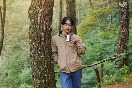 Portrait of excited Asian hiker man drinking water from stainless steel cup while trekking in nature forestの写真素材