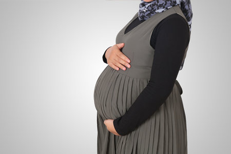 Cropped portrait of unrecognizable pregnant muslim woman with hands over tummy. Isolated image on white backgroundの写真素材