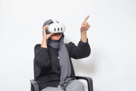 Portrait of Asian woman with hijab using virtual reality VR device, experiencing immersive technology. Isolated image on white backgroundの写真素材