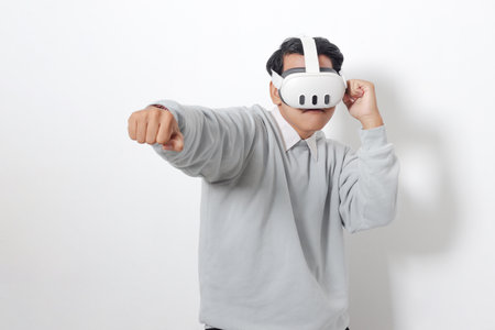 Portrait of Asian man using virtual reality VR device, trying to punch and fight his enemy in game. Isolated image on white backgroundの写真素材