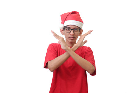 Portrait of excited Asian man in red t-shirt with santa hat showing X sign of hands. Teenager refusing an invitation from someone. Isolated image on white backgroundの写真素材