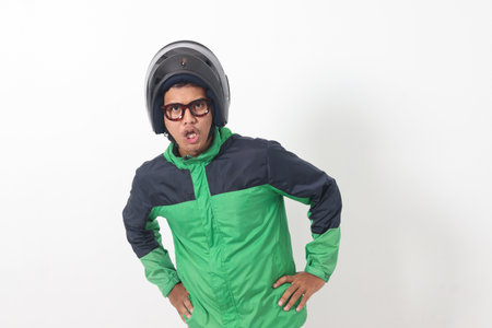 Portrait of tired Asian online taxi driver wearing green jacket and helmet doing weird funny pose. Isolated image on white backgroundの写真素材