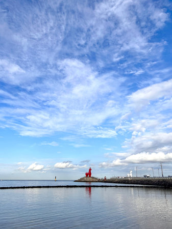 Seascape with a red lighthouse and a blue sky with clouds