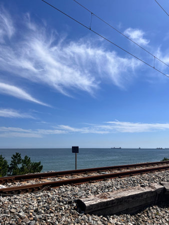 Railway tracks leading to the sea and blue sky with white cloudsの写真素材