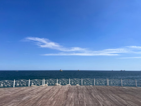 Wooden platform on the sea with blue sky and ships in the backgroundの写真素材