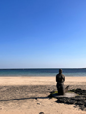 Statue of a woman sitting on the beach with blue sky background
