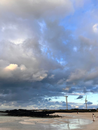 Wind turbines on the beach at sunset with clouds and blue sky.