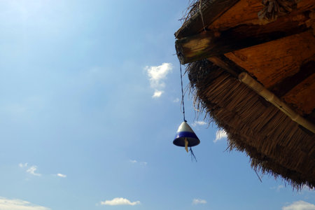 Blue and white bell hanging from the roof of a hut with blue skyの写真素材
