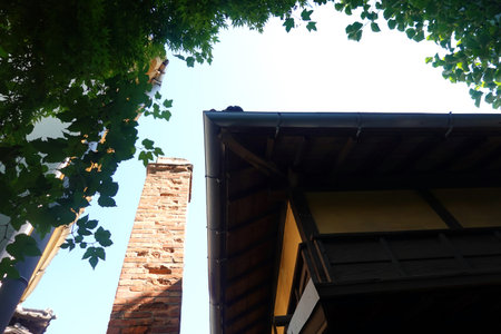 Roof of old house with blue sky and green leaves in the garden