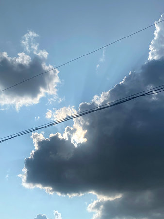 High voltage power lines against the blue sky with clouds and sun rays