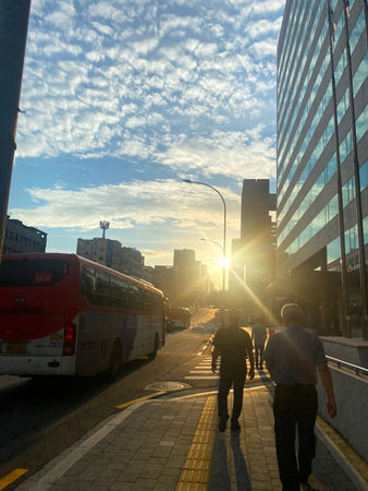 Busy city street at sunset, with people walking and passing by