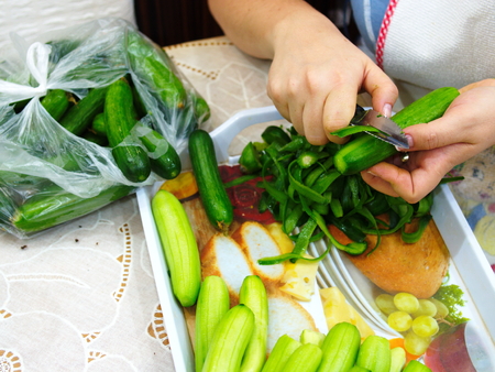 prepare a salad. cleanses cucumber shells with women's hands. cucumber is cleaned with a peeling knife. Preparing for mealsの写真素材