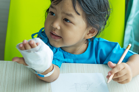 Illness little asian kids writing paper on desk in hospital, saline intravenous IV on handの写真素材