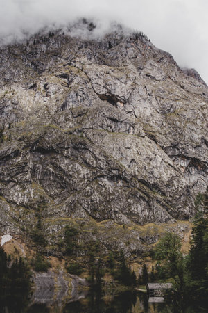 Obersee. Bavaria. Germany. Rock mountain wall, pines & wooden shipyard reflect in lake's water in...