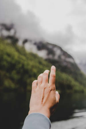 Palm of hand on background of river, green forest, mountain & gray clouds. Vertical wallpaperの写真素材