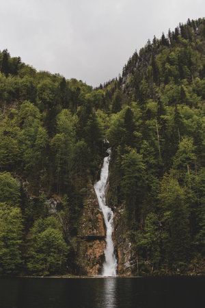 Schrainbach waterfall falls into Konigssee lake from the rock mountain covered by dense forest on...