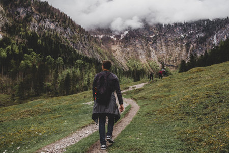 Tourist man hikes to Rothbach waterfall throw pine forest on background of rock mountains & cloud sky. Bavaria. Germanyの写真素材