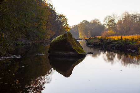 Boulder in river and autumn trees on the rivers coastの写真素材